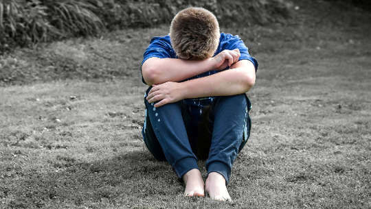 boy sitting on the sand with his head on his knees