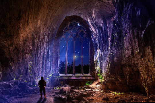 a man in a cave with a huge arch opening to the night and sky