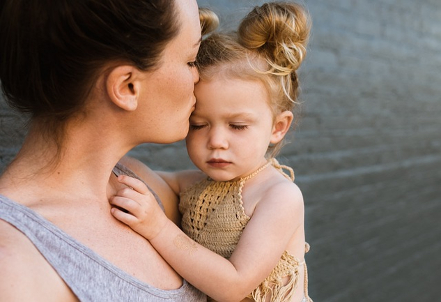mother holding her young child and kissing her on the forehead