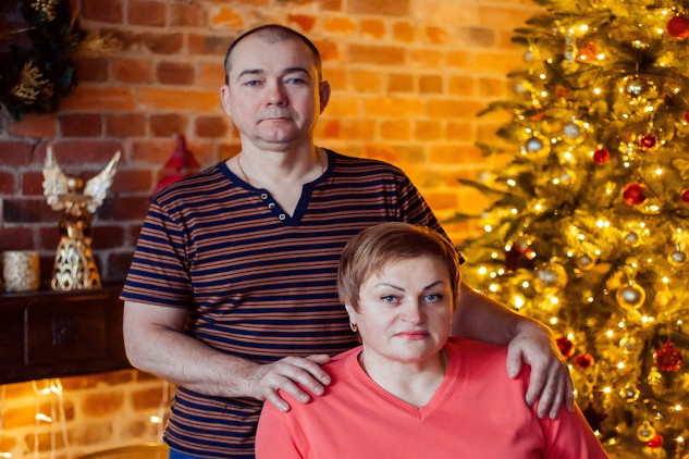 a portrait of an unhappy looking couple, her sitting and him standing his hands pressing down on her shoulders