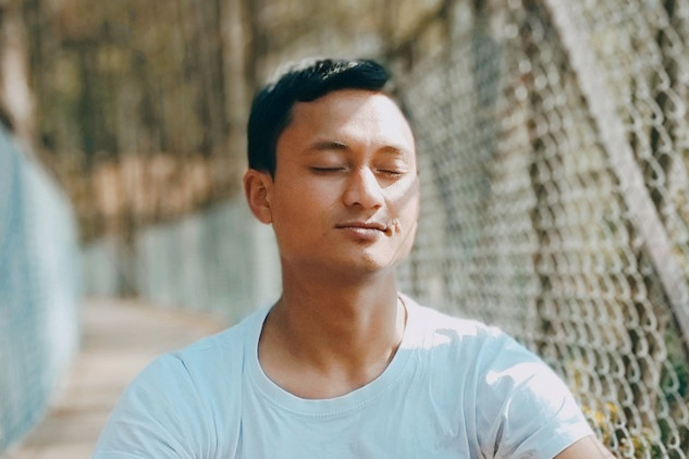 a man with a peaceful smile sitting in meditation pose outside on a bridge
