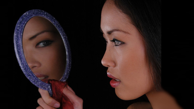 a woman looking at herself in a hand-held mirror