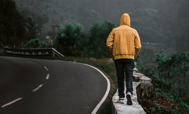 a man on a solitary walk on a path next to a paved road