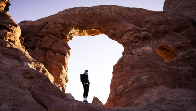 A man standing in a the bright space of an arch amidst rock. Image by Eric Barrett from Pixabay.